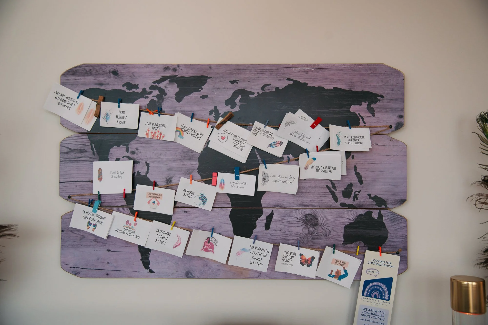 World map on purple wooden background with inspirational messages on white cards clipped to twine, hung in a wave pattern