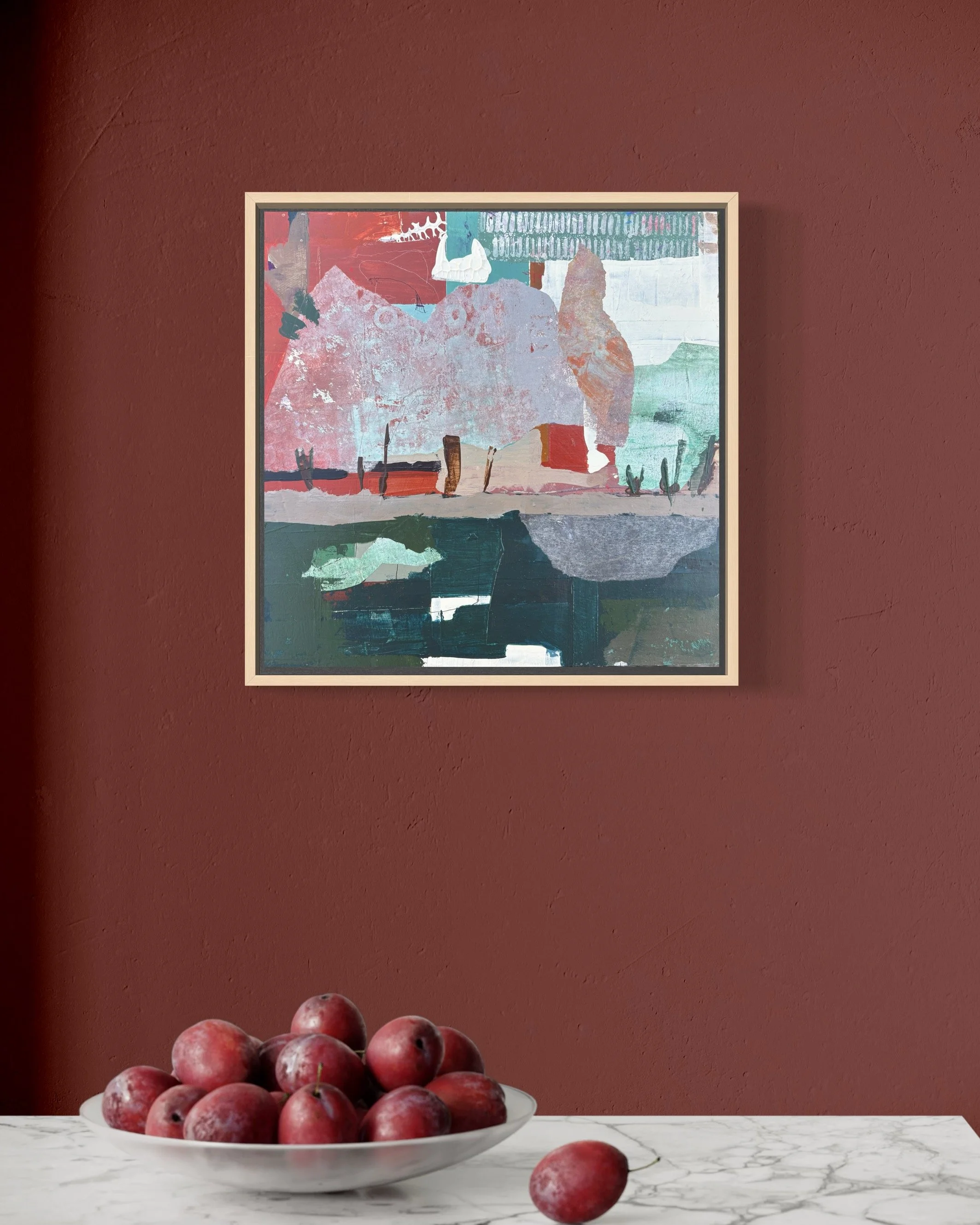 A bowl of red grapes on a white marble surface in front of a red wall with an abstract painting hanging on it.