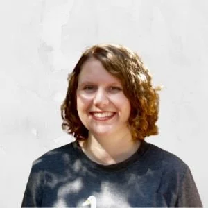 A young woman with curly brown hair smiling against a plain white background.