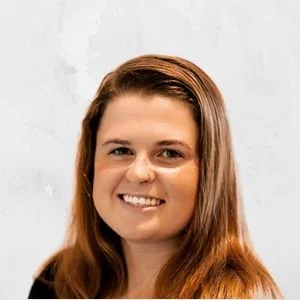 Portrait of a smiling woman with long reddish-brown hair against a light gray background.