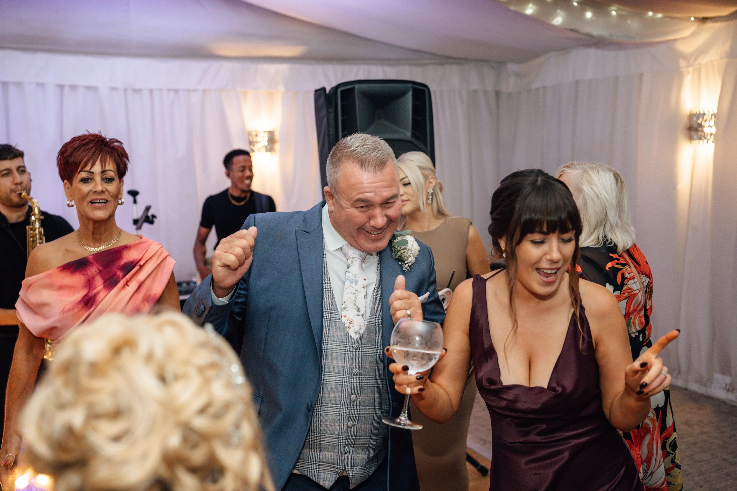 People dancing and celebrating at a wedding reception inside a white tent with soft lighting.