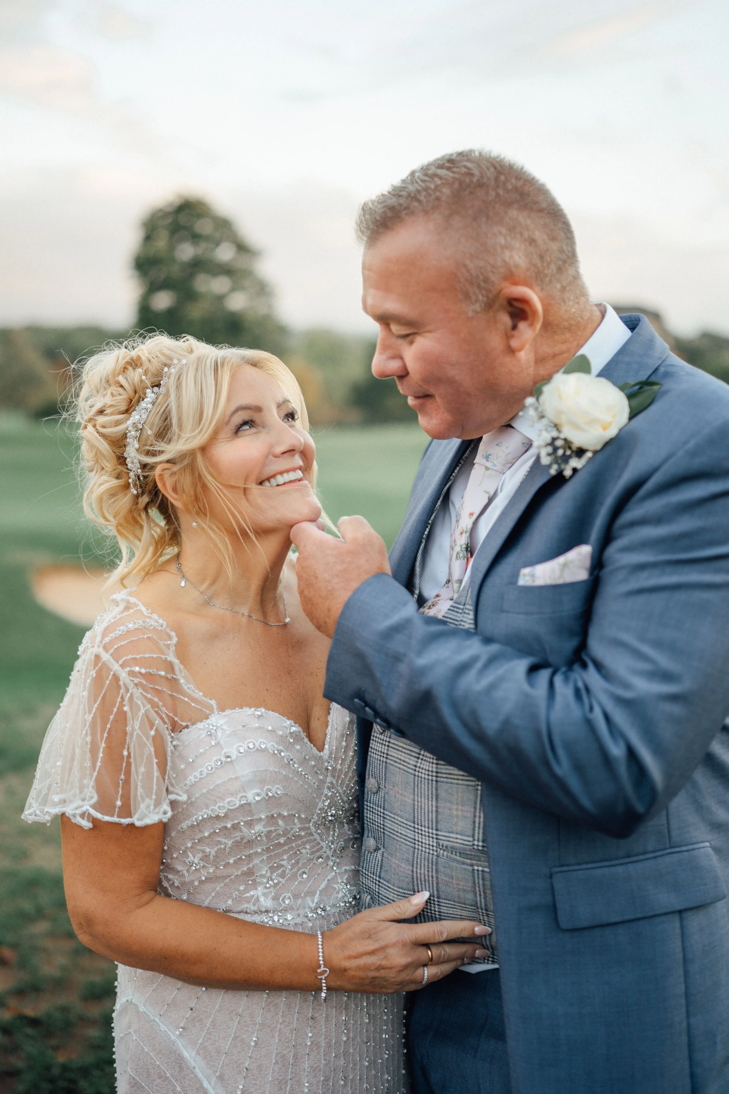 A bride and groom share an intimate moment outdoors at their wedding, gazing into each other's eyes and smiling.