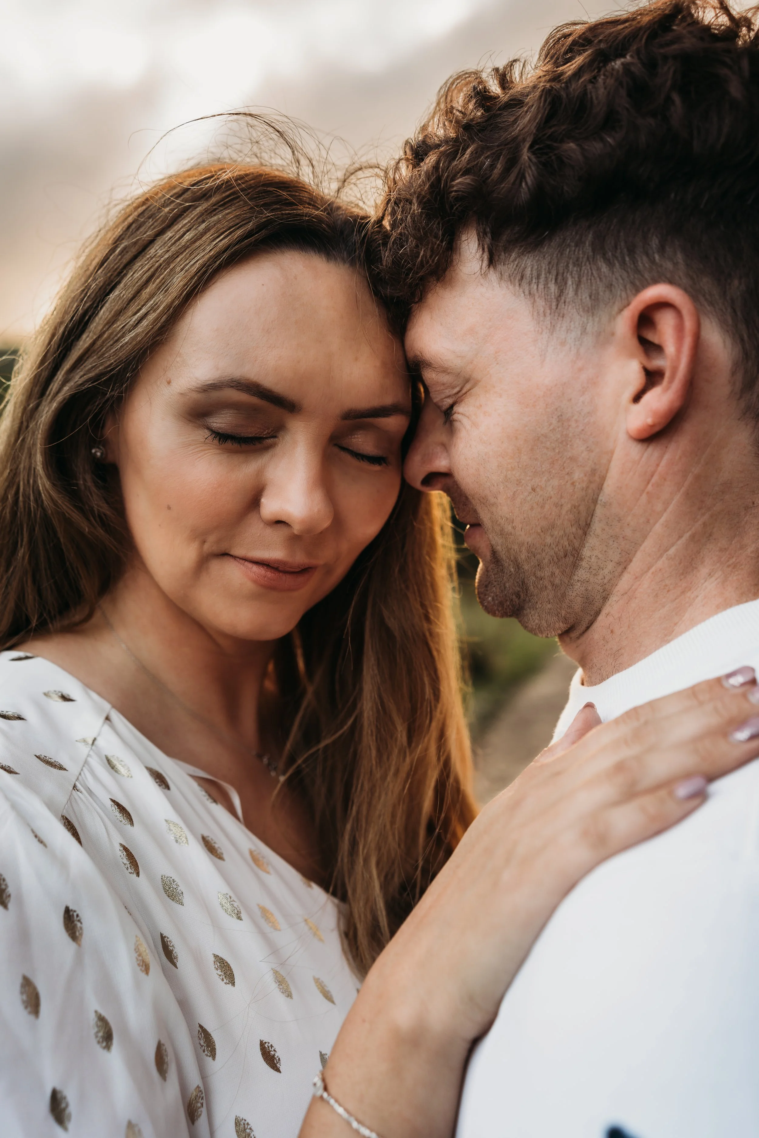 A couple with foreheads touching, eyes closed, outdoors during sunset, intimate moment.