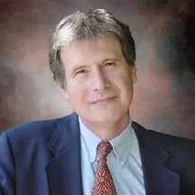 Smiling man with gray hair wearing a blue shirt, blue suit and red tie.