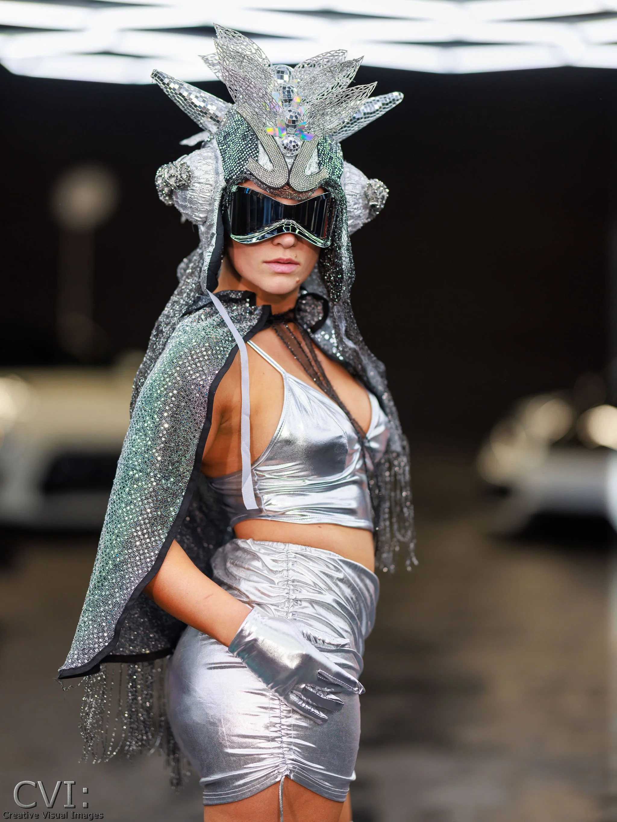 Woman dressed in metallic silver outfit with a futuristic headdress and goggles, standing in an urban setting.