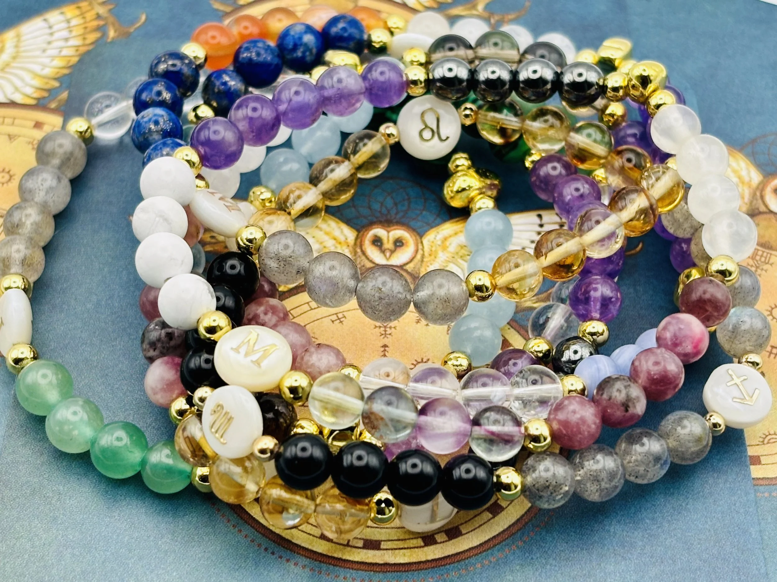 Close-up of multiple beaded bracelets with various colors and styles, some featuring alphabet letter beads, arranged on a patterned cloth.