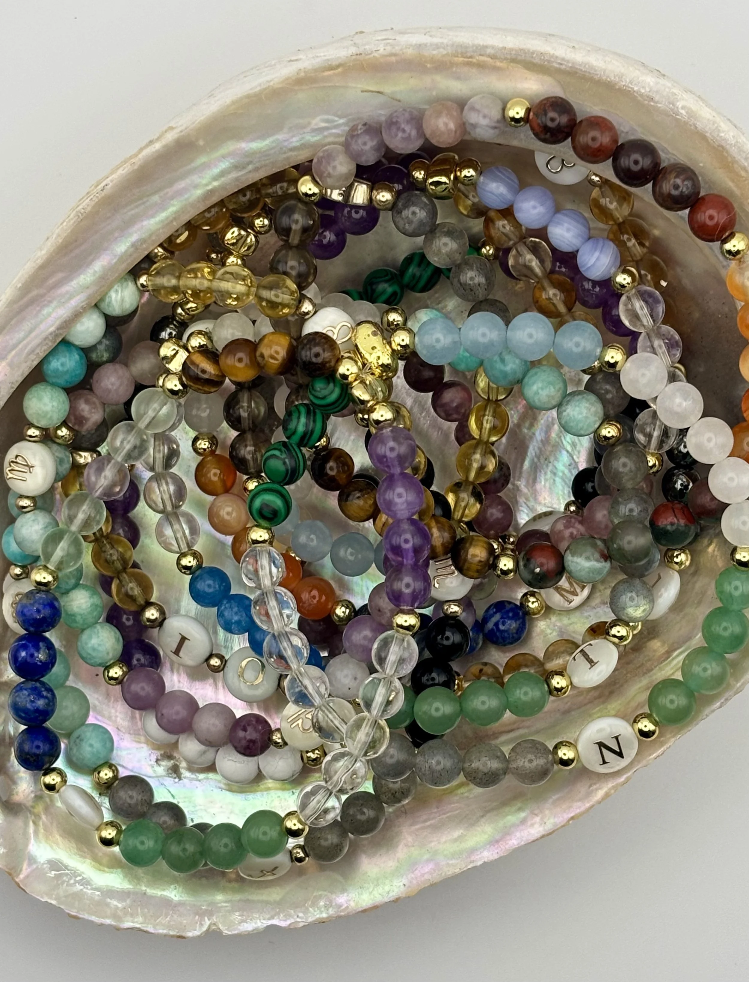 A collection of colorful beaded bracelets inside a large shell with an iridescent surface.
