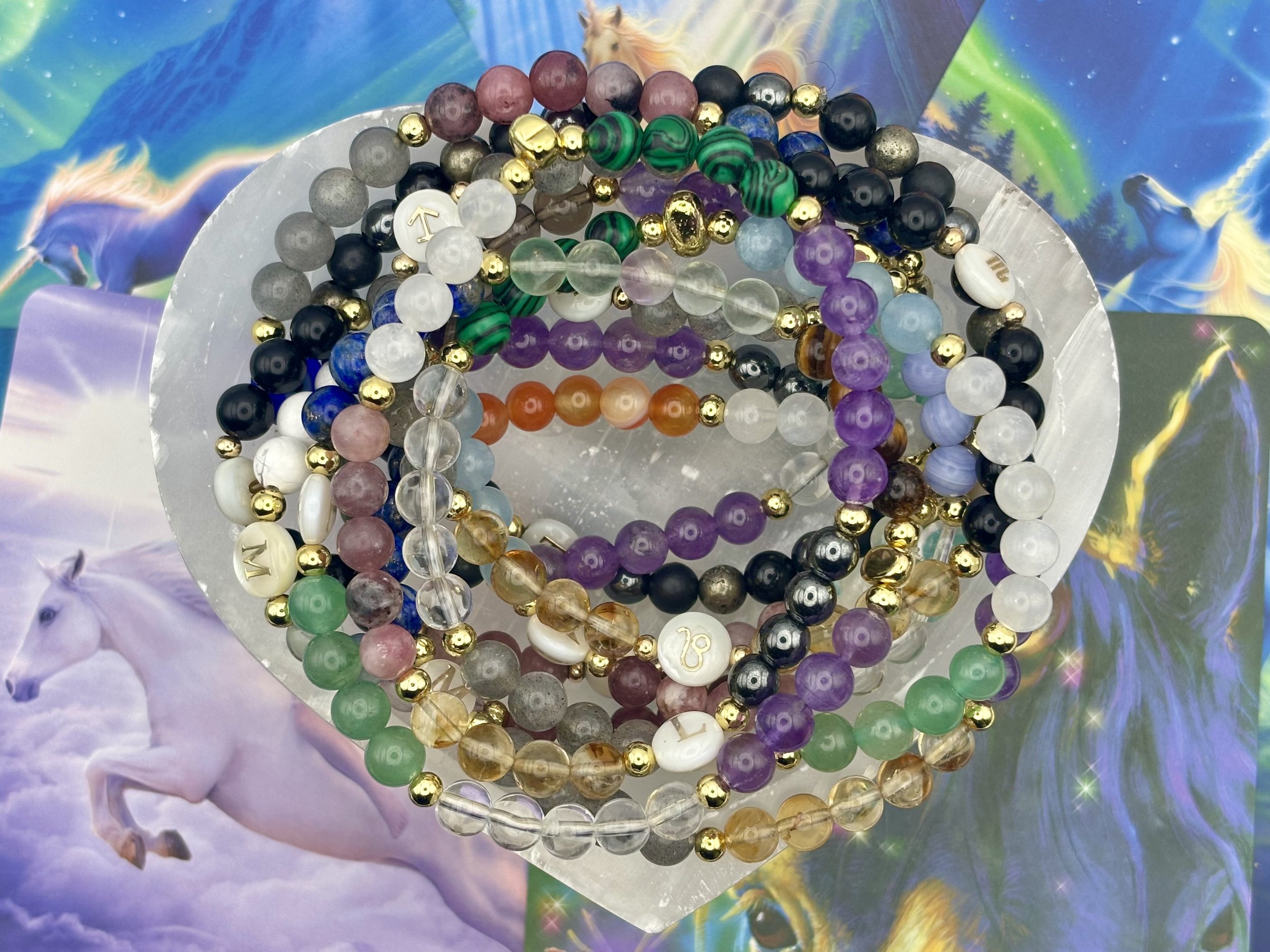 Colorful bead bracelets with various patterns and metallic accents, placed on a reflective silver surface, against a dreamy, pastel, fantasy-like background with aurora borealis and horse images.