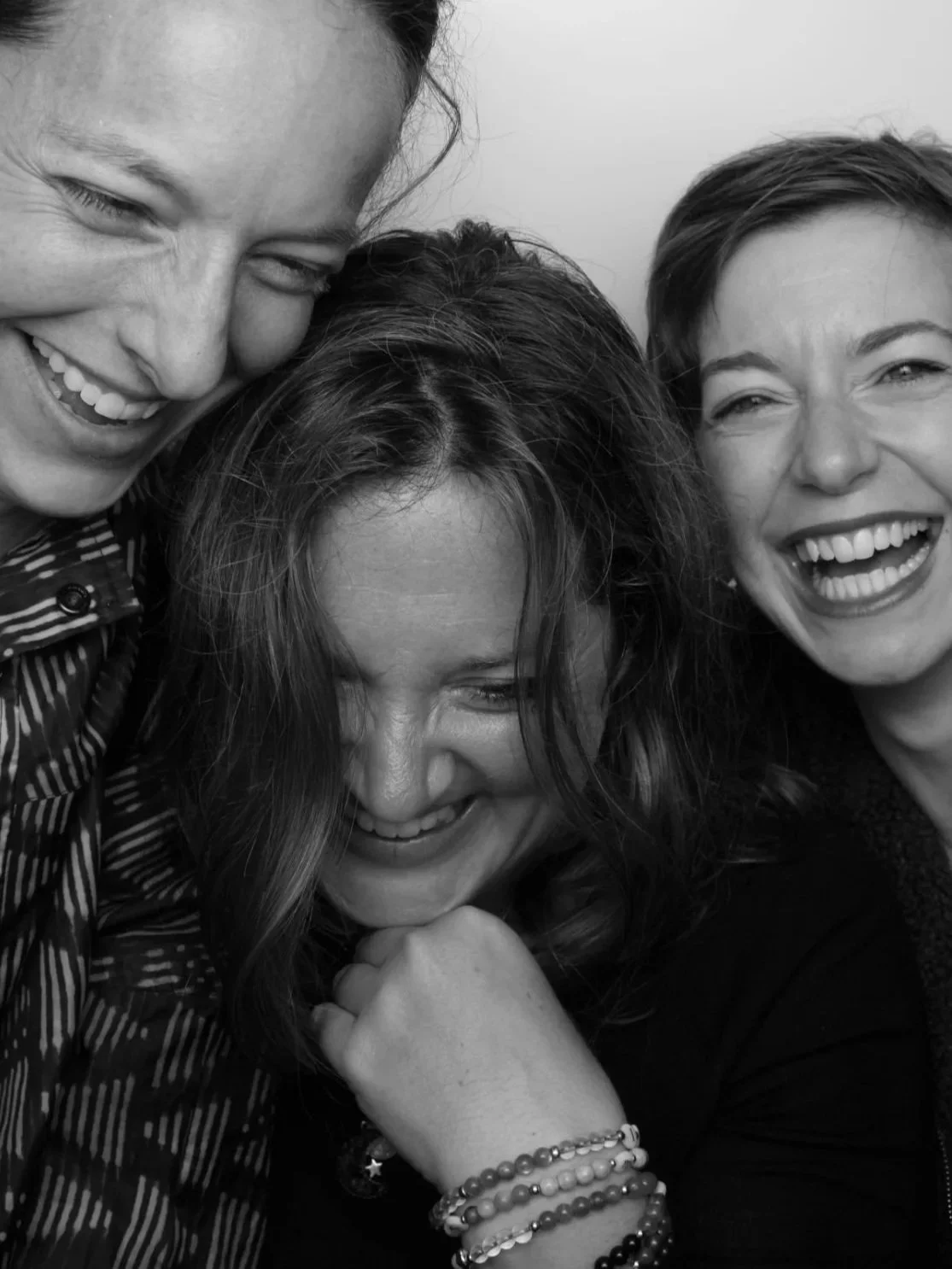 Three women laughing and smiling closely together in black and white photo.