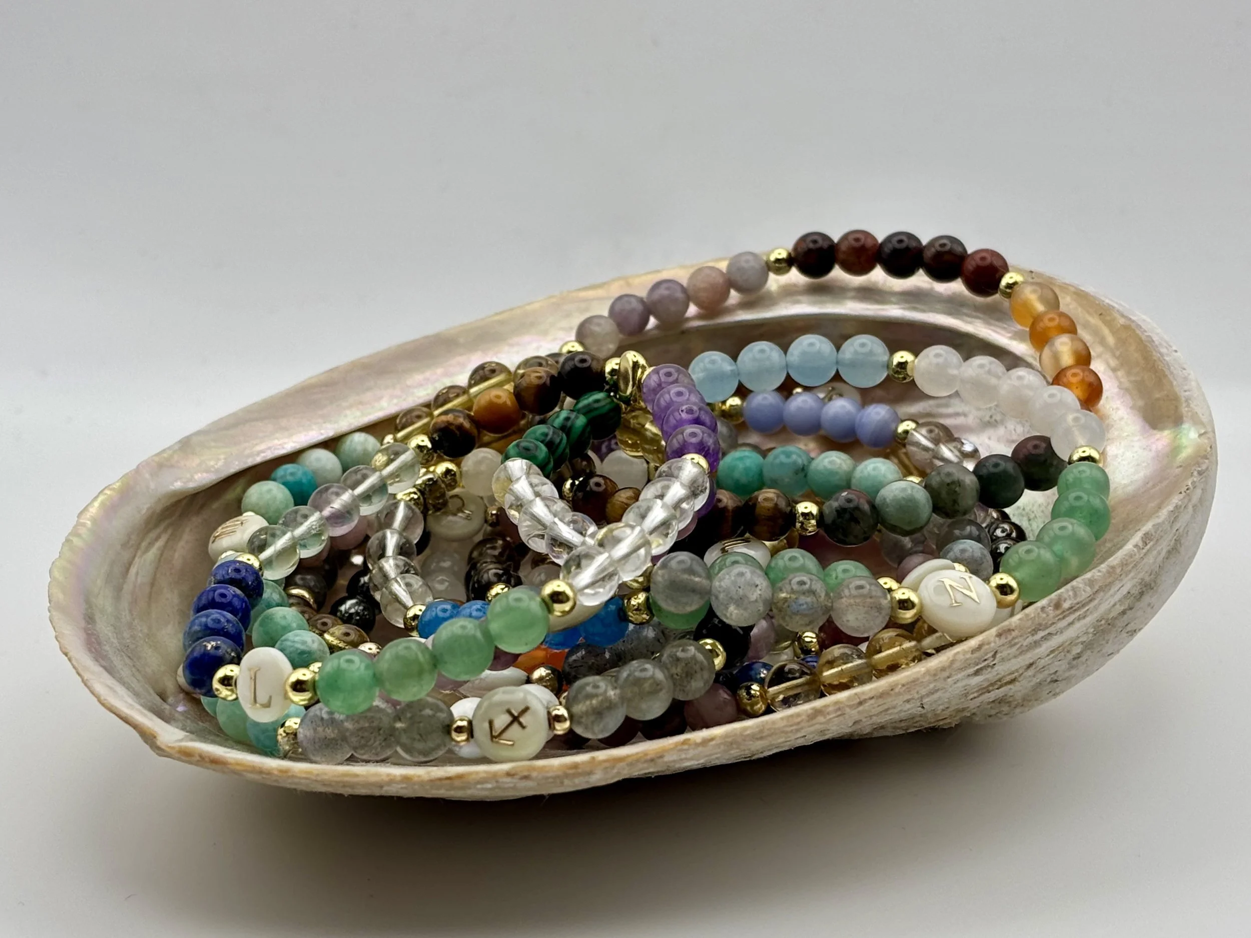 Multiple beaded bracelets in various colors and styles inside a shell-like dish.