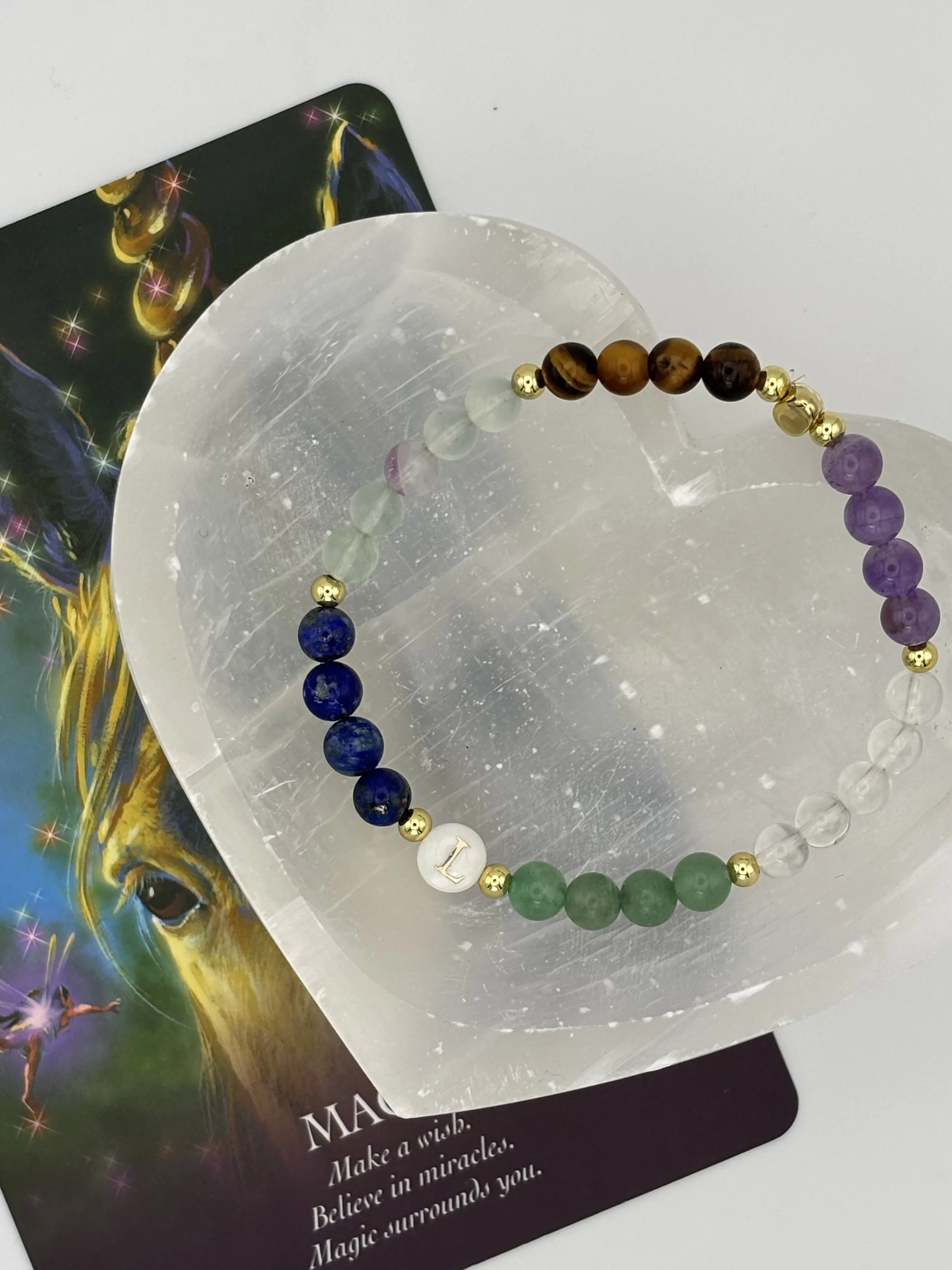 Colorful bracelet with multicolored beads, positioned on a reflective surface, with part of a card beneath it.
