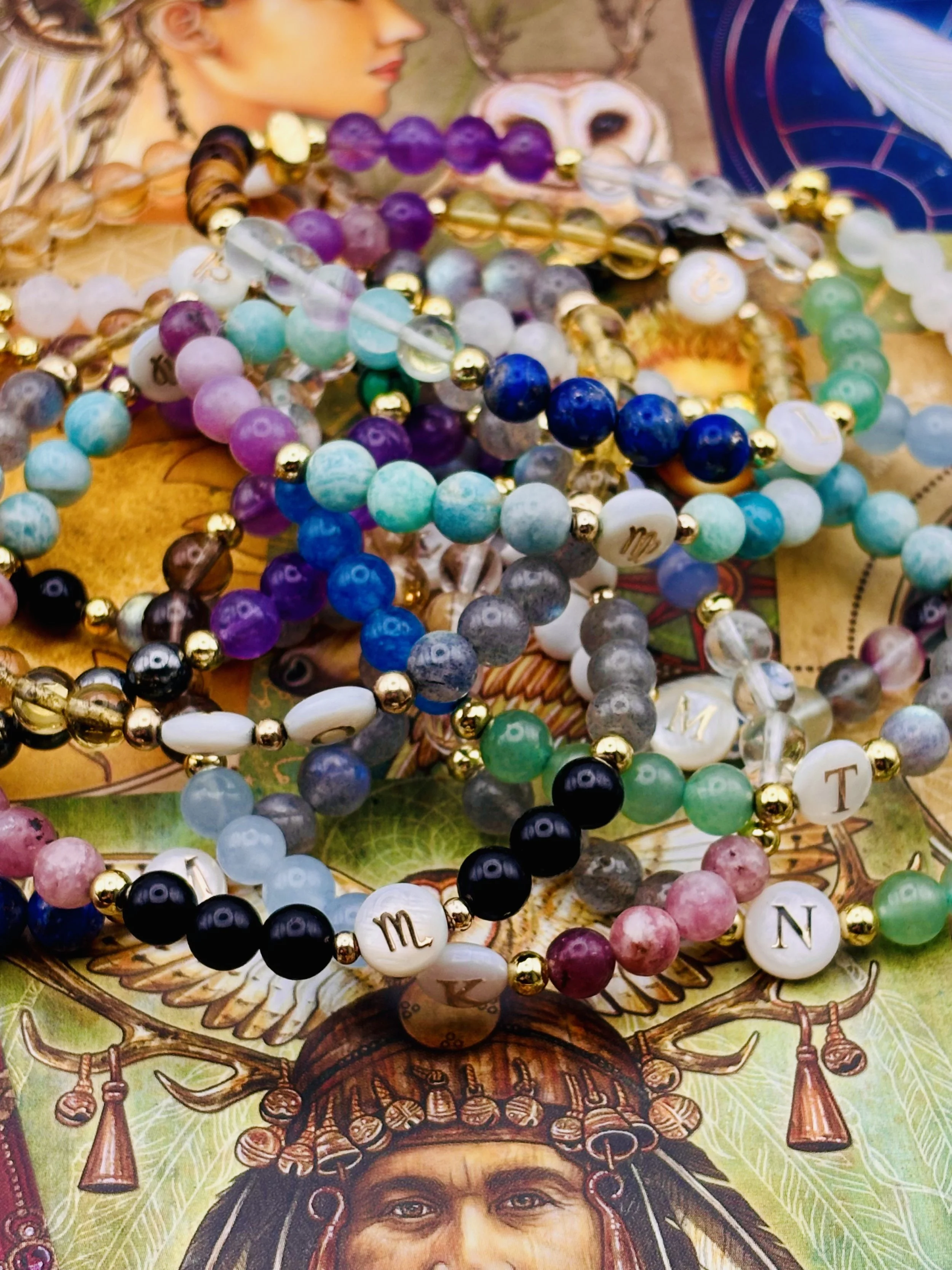 Close-up of colorful beaded necklaces with various colors and sizes, some with lettered beads, layered over a detailed artwork of a person's face with traditional jewelry and face paint.