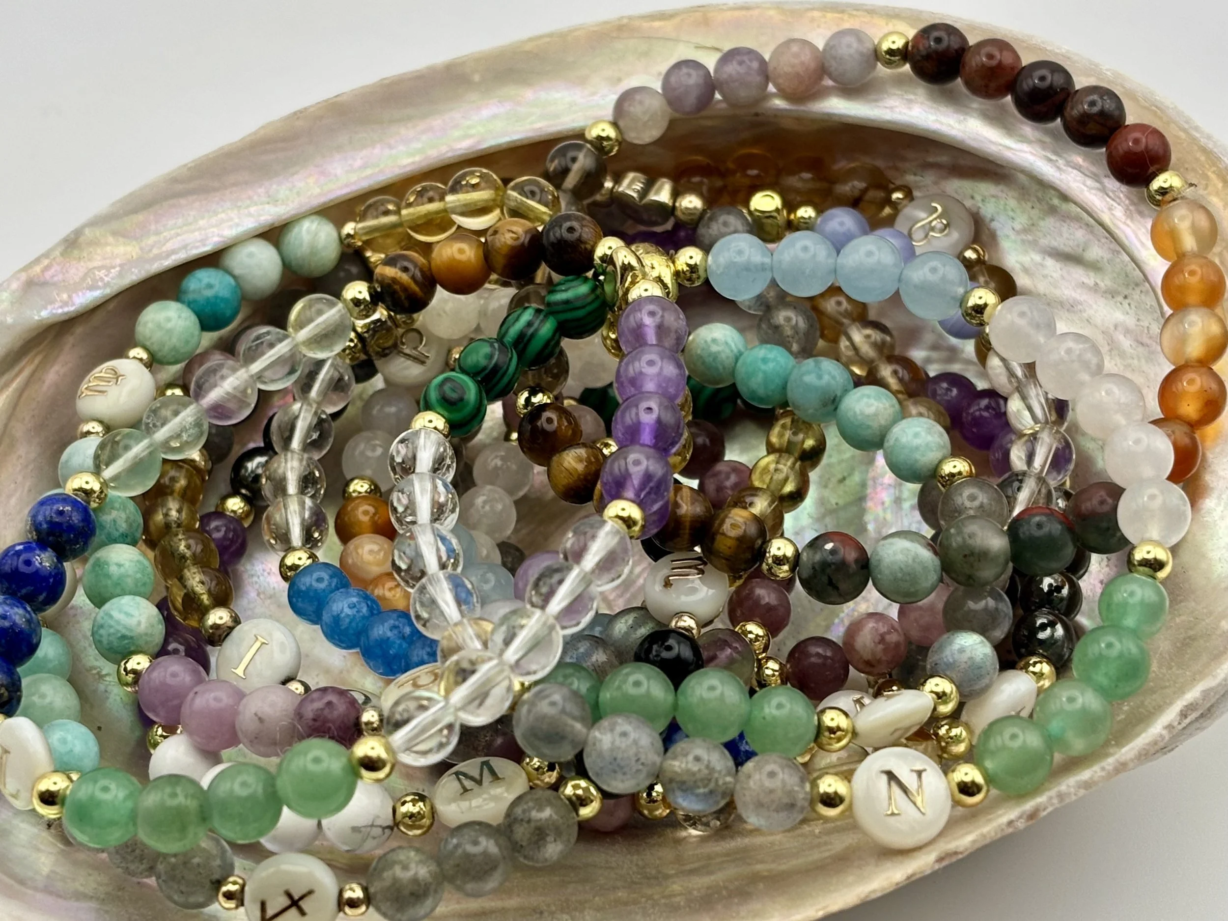 A collection of colorful beaded bracelets, including gold, pearl, and gemstone beads, displayed in a shell-shaped container.