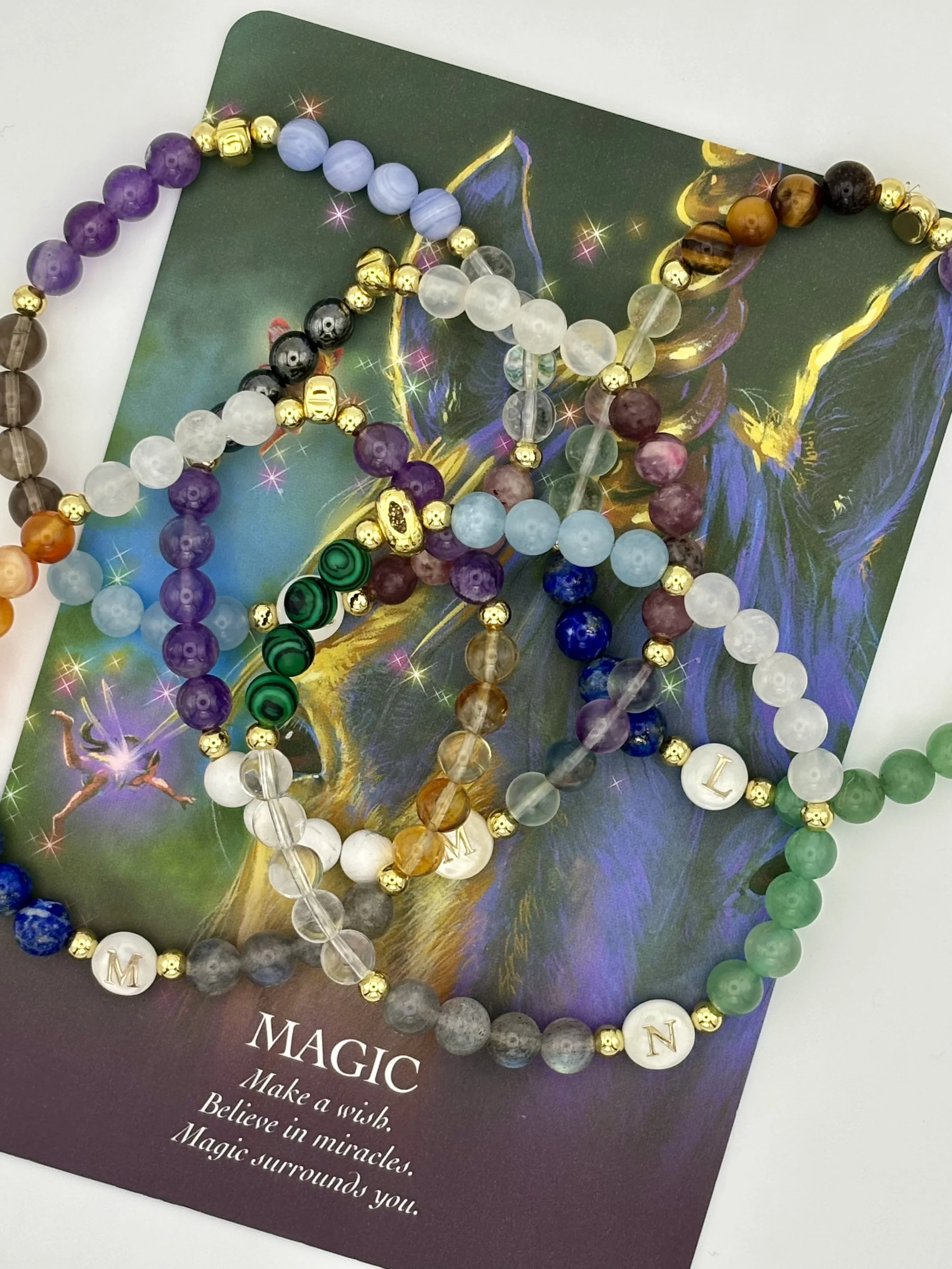 Three beaded bracelets with varying colors and patterns, resting on a colorful motivational card with the word "MAGIC" and an inspirational message.