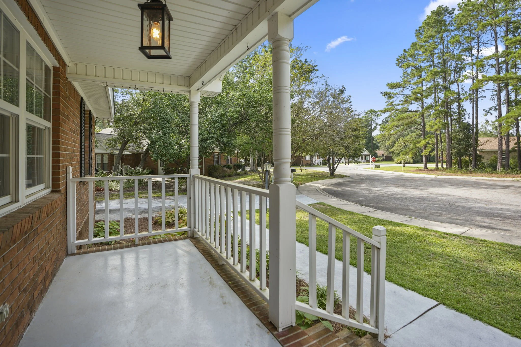 View from a porch overlooking a suburban neighborhood with trees, grass, and a curved street under a clear blue sky.