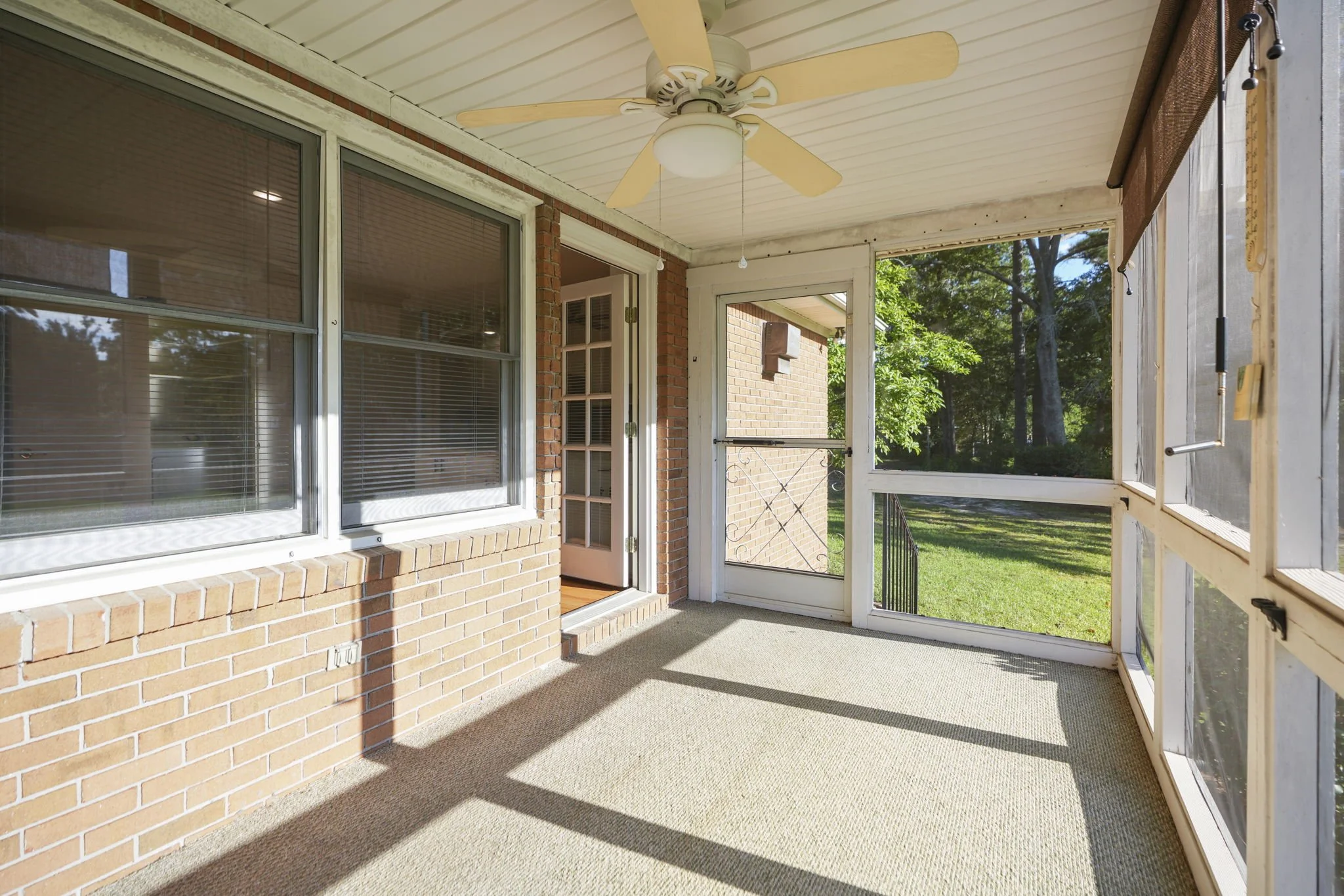 Enclosed porch with brick walls, large windows, ceiling fan, and view of green yard and trees outside.