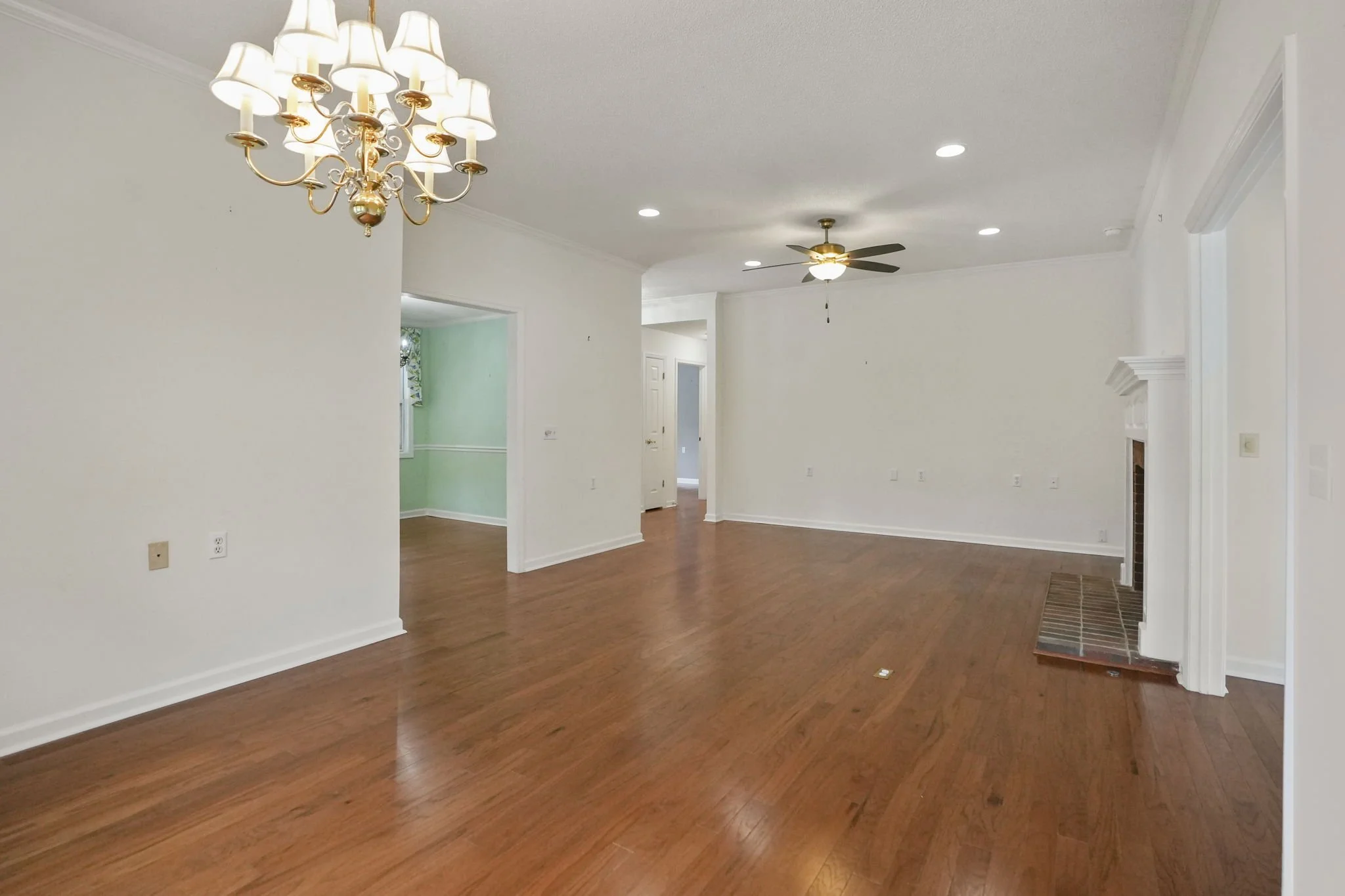 Empty living room with hardwood floors, white walls, a chandelier, a ceiling fan, and a fireplace.