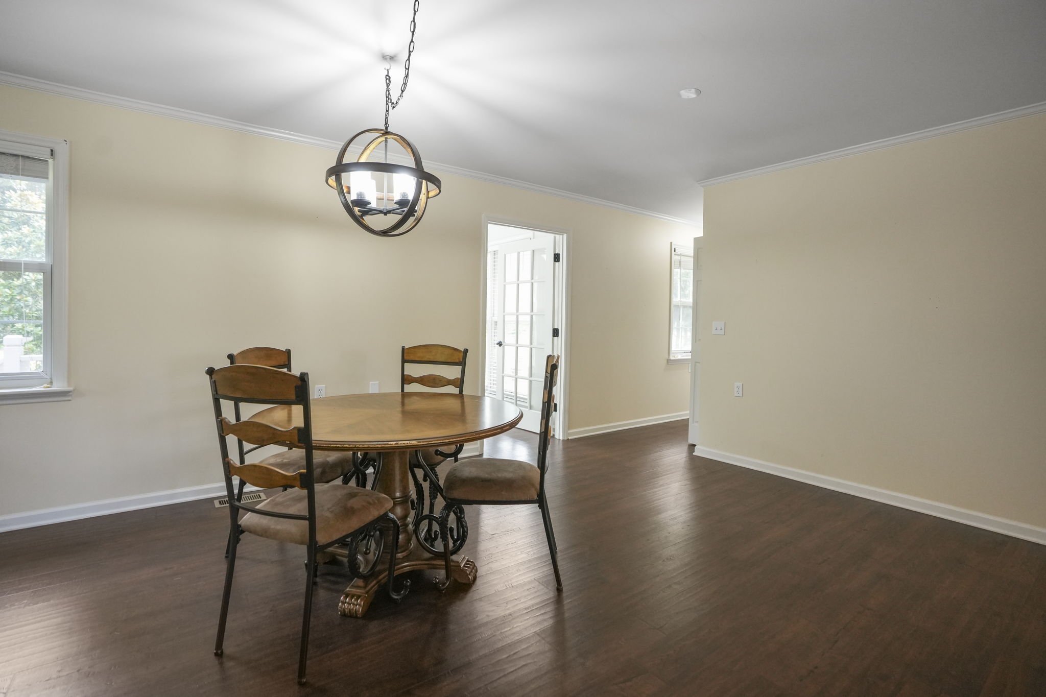 Empty dining room with a wooden table and four chairs, a modern chandelier, and wooden flooring.