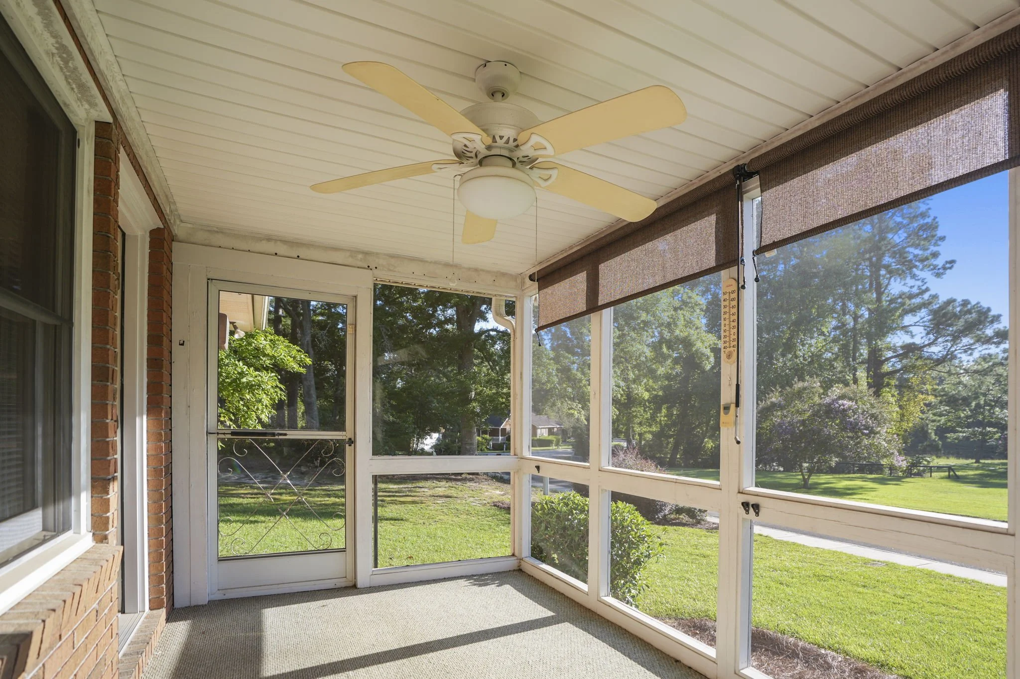 Sunroom with screened windows, ceiling fan, and view of a green yard with trees and bushes.