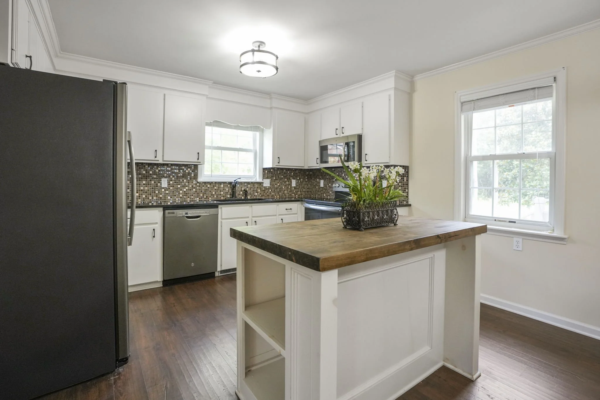 Kitchen with white cabinets, a wooden island, mosaic tile backsplash, stainless steel appliances, and a window letting in natural light.