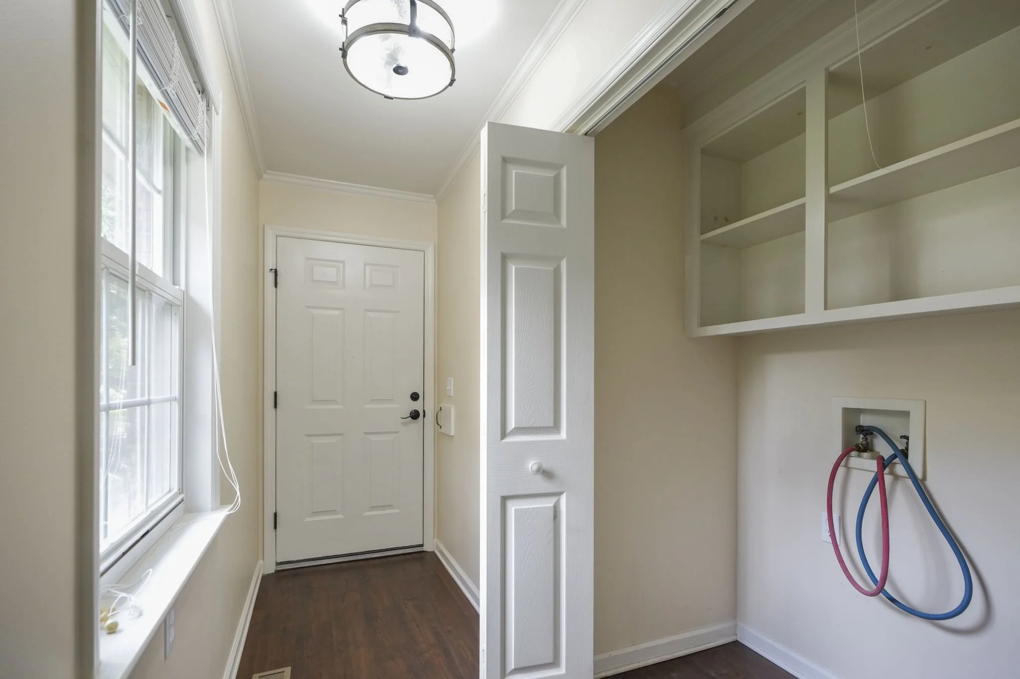 Empty laundry room with a white door, a window, open cabinetry, and plumbing hookups for a washer and dryer.