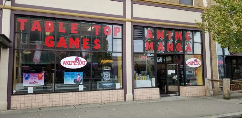 Storefront with large window displays and signage for 'Table Top Games' and 'Anime Manga' in red lettering, with promotional posters visible in the window.