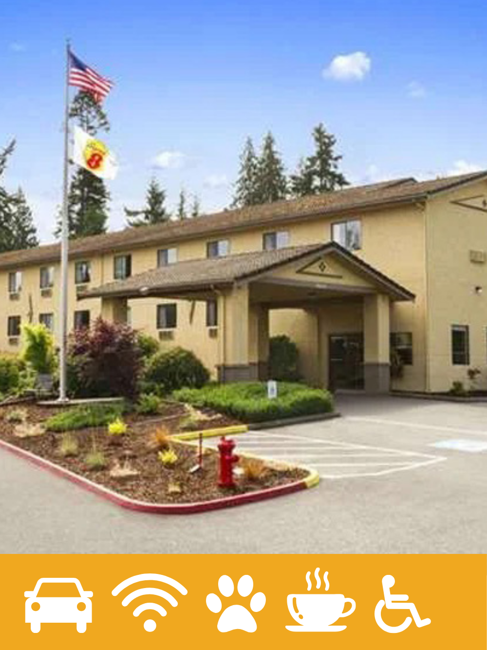 Exterior of a yellow motel or hotel building with a parking lot, American flags, and surrounding greenery, under a partly cloudy sky.