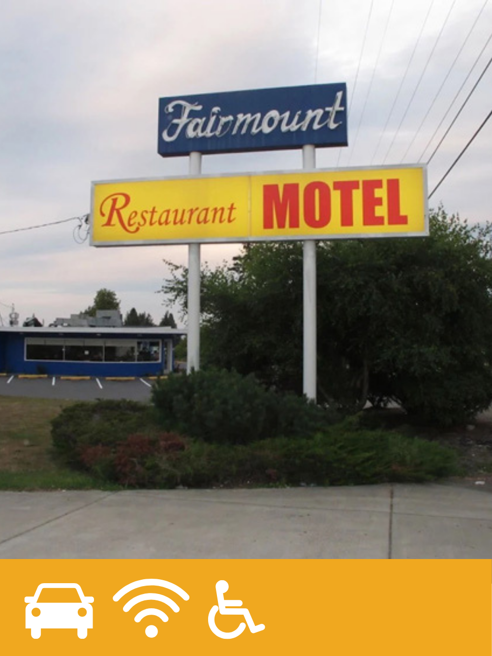 Signboard for a motel with a restaurant, located in a parking lot with bushes in front and a building in the background.