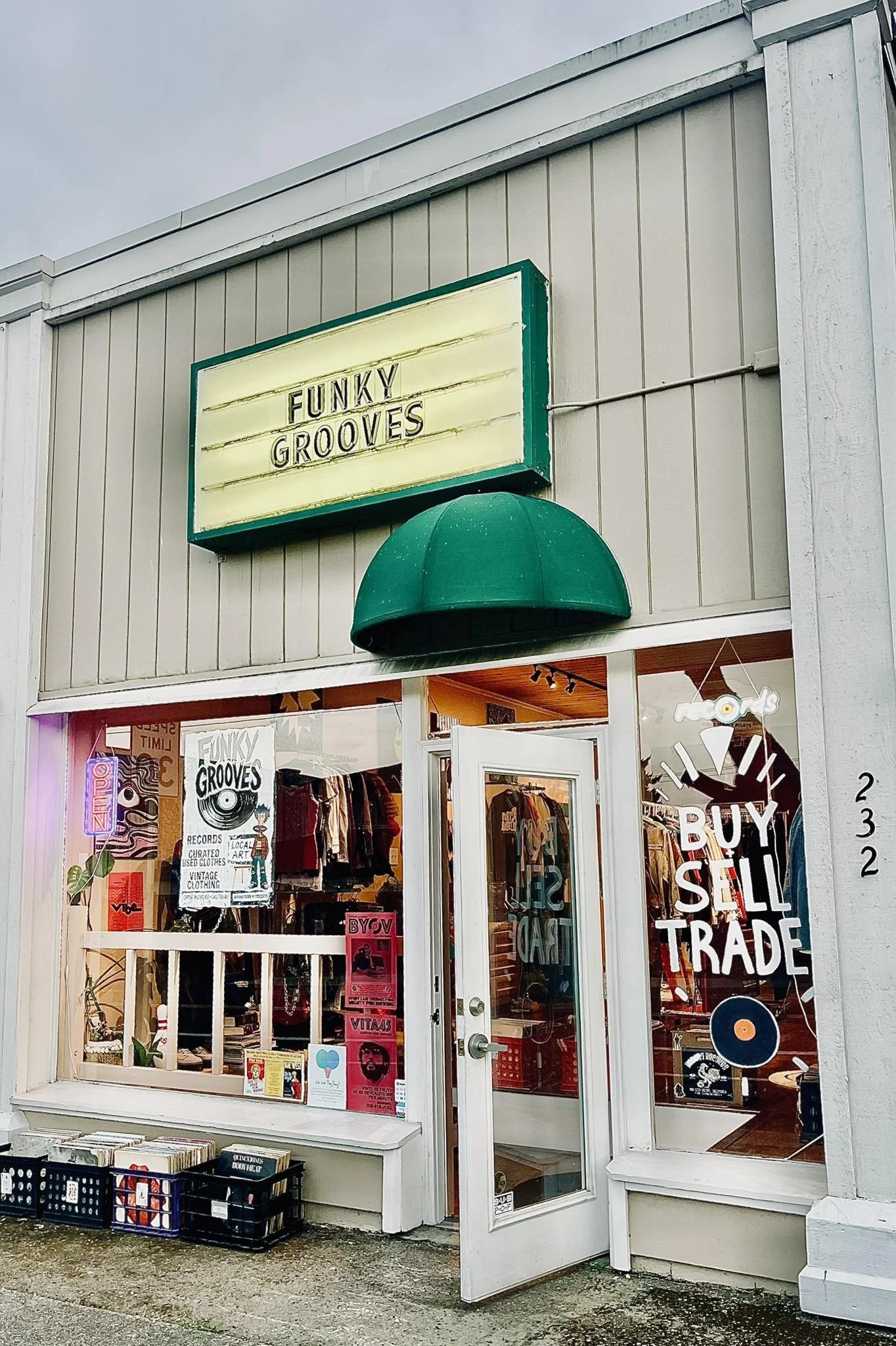 Front view of a vintage clothing store named 'FUNKY GROOVES' with a neon signs and posters in the window, displaying 'BUY SELL TRADE'.