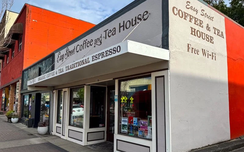 Exterior of Easy Street Coffee and Tea House, a small coffee shop with white walls, black trim, and signage advertising coffee, tea, and free Wi-Fi, situated on a sidewalk in a commercial area.