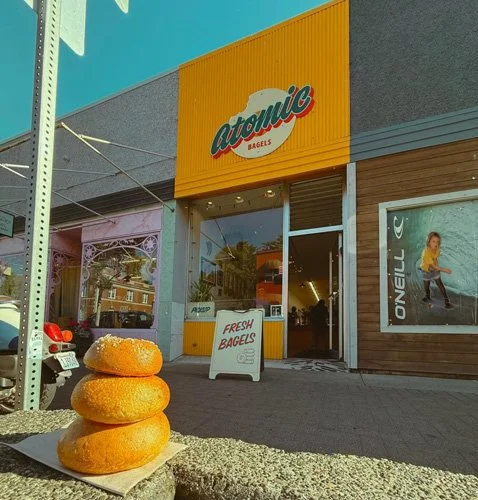 Stacked bagels with sesame seeds outside a bagel shop named Atomic Bagels.