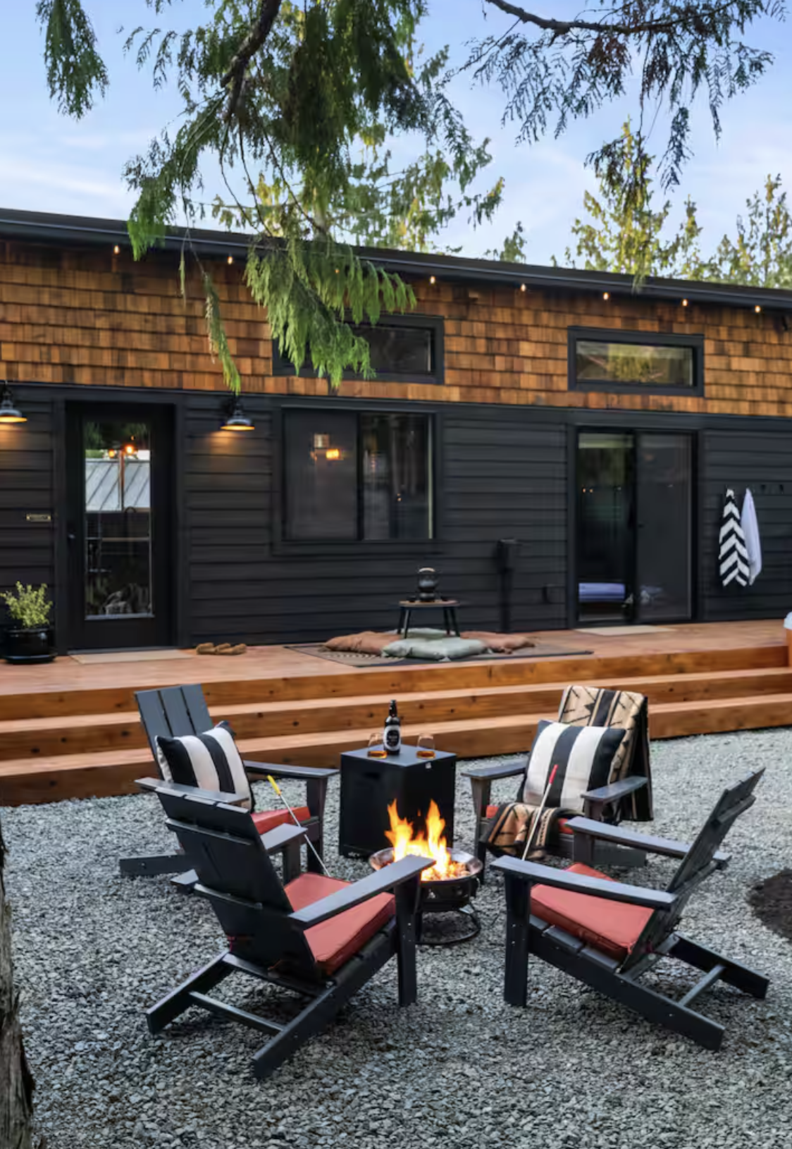 The outside of The Sugi Box Air Bnb in Port Angeles, featuring a charcoal-colored and wood decorated tiny home with a firepit seating area outside.