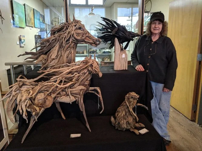 Woman standing next to wooden sculptures of horses and a bird in an art gallery.