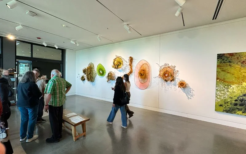 People viewing a series of colorful, abstract art sculptures on a white wall in an art gallery.