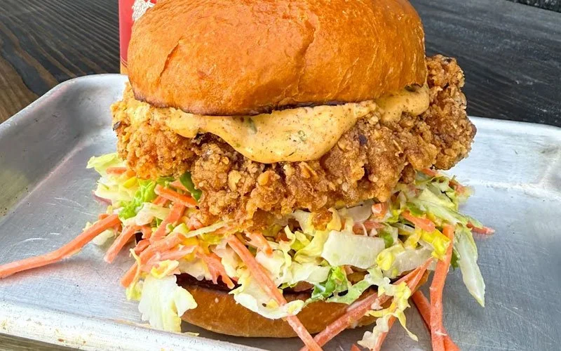 Fried chicken sandwich with lettuce, coleslaw, and sauce in a bun