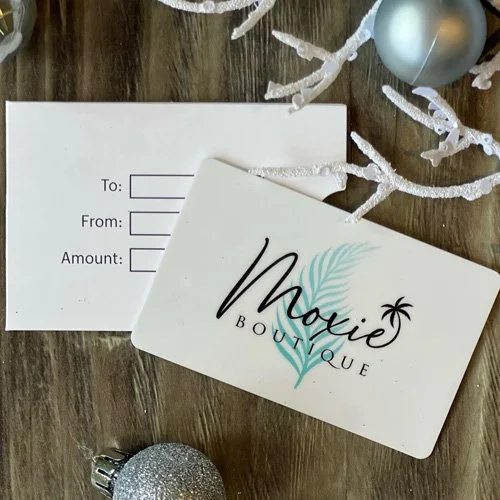 A gift card for Movie Boutique with a floral design, alongside a matching paper and Christmas ornaments on a wooden surface.