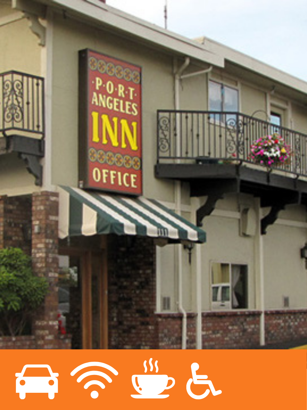 Exterior of a small building with a sign that reads 'Port Angeles Inn Office'. The building has a balcony with pink flowers, brick and stucco walls, and a green and white striped awning over the entrance.