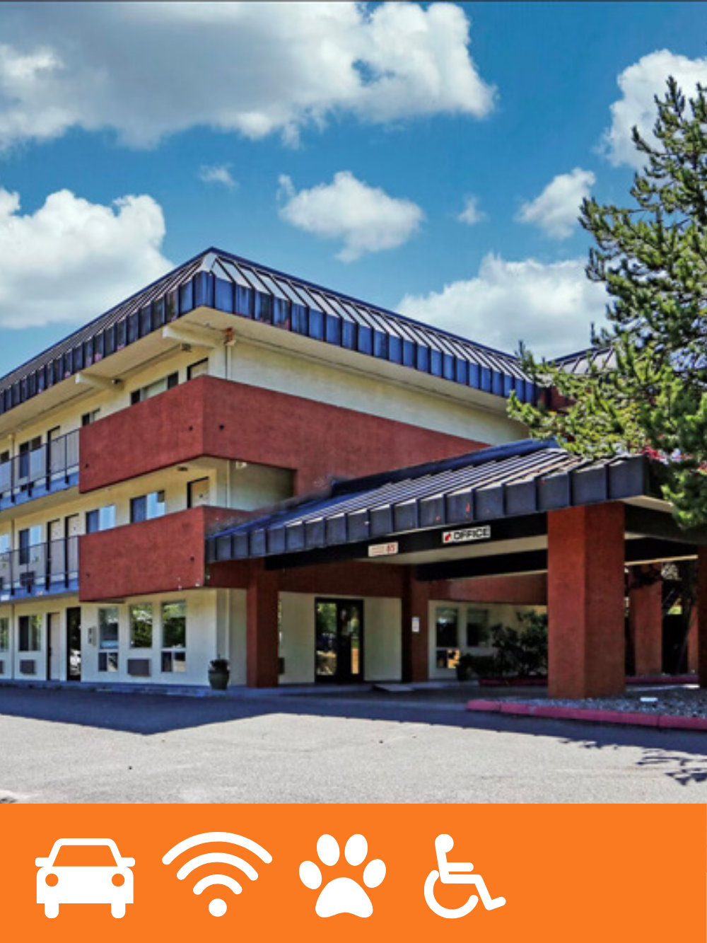 A three-story office building with a blue-tiled roof, red and cream exterior walls, surrounded by a parking lot, a tree, and a partly cloudy sky.