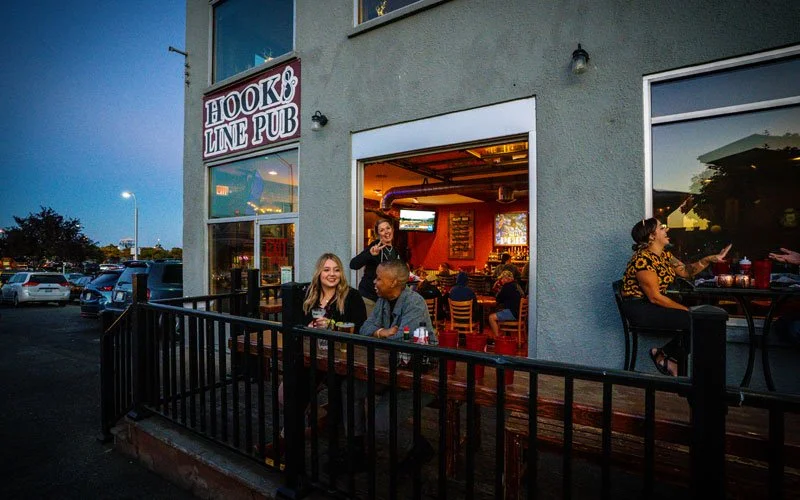 People sitting outside Hook & Line Pub at dusk, some enjoying drinks, with the pub's lit interior visible through the open door.