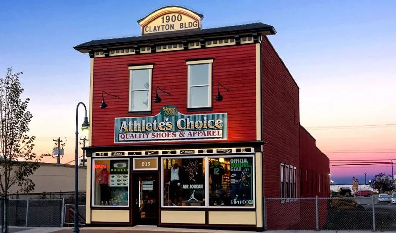 A two-story red building with a sign reading '1900 Clayton Bldg' on the roof and a storefront labeled 'Athlete's Choice, Quality Shoes & Apparel'.