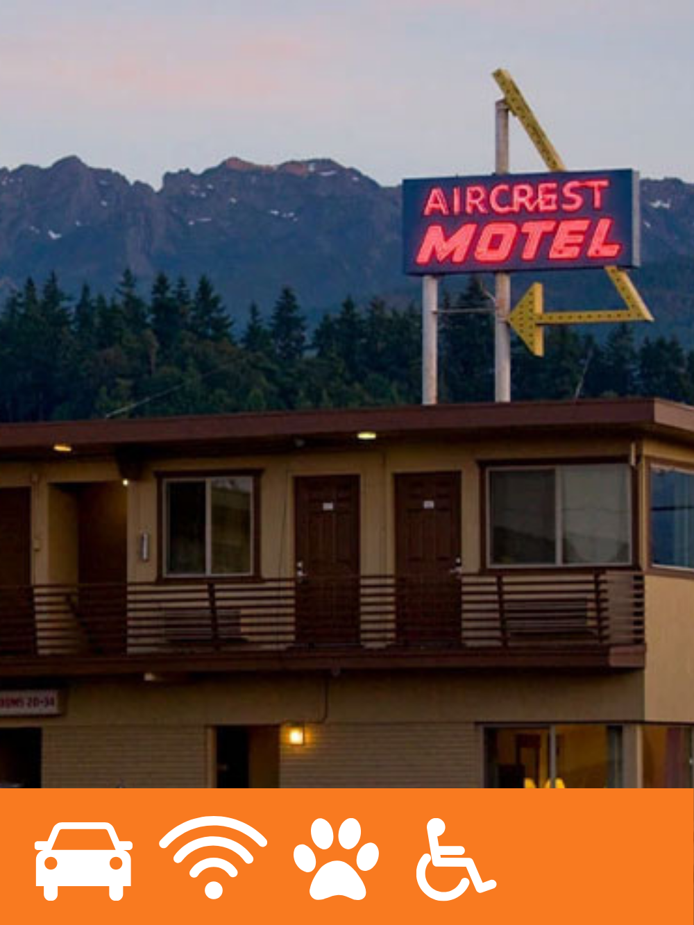 Vintage motel sign reading 'Aircrest Motel' with a mountain range and trees in the background during dusk.