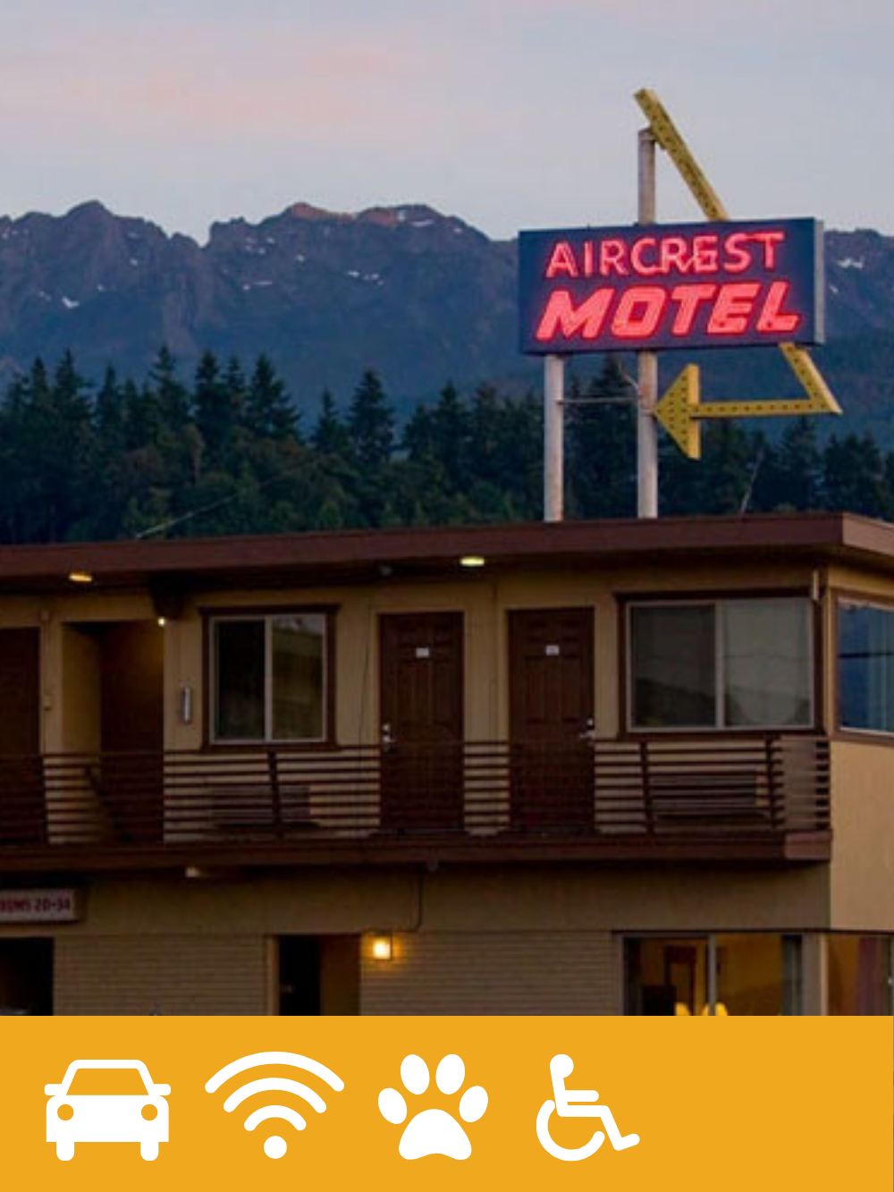 Vintage motel sign reading 'Aircrest Motel' with a mountain range and trees in the background during dusk.