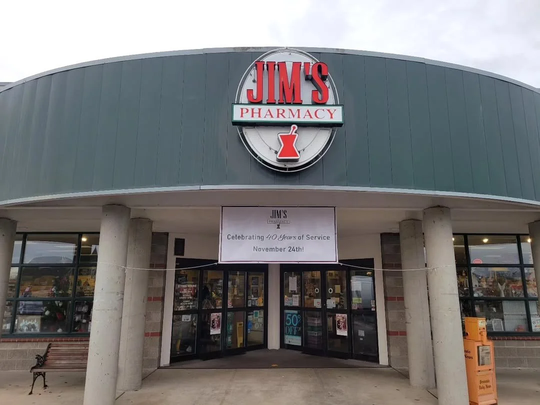 Front view of Jim's Pharmacy store with a large sign above the entrance and a banner celebrating 40 years of service.