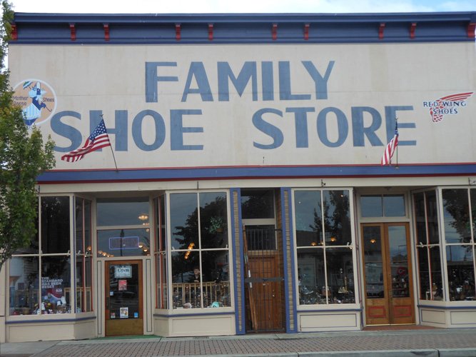 Facade of a family shoe store with large blue lettering, American flags, and vintage-style windows.