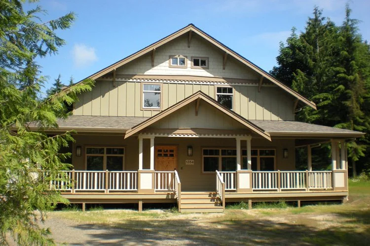 Large two-story house with a front porch, surrounded by green trees, under a blue sky.