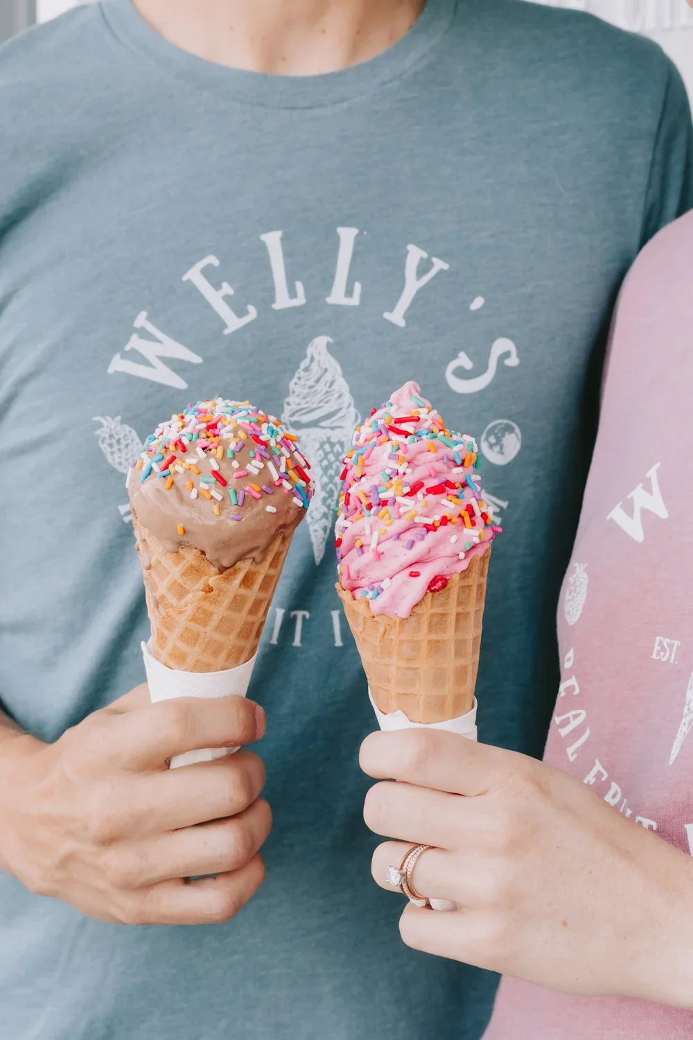 Four people sitting on a wooden bench, enjoying ice cream cones in front of a colorful mountain mural and trees.