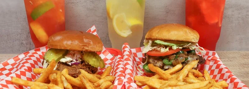 Two cheeseburgers with fries and three colorful beverages on a wooden table.