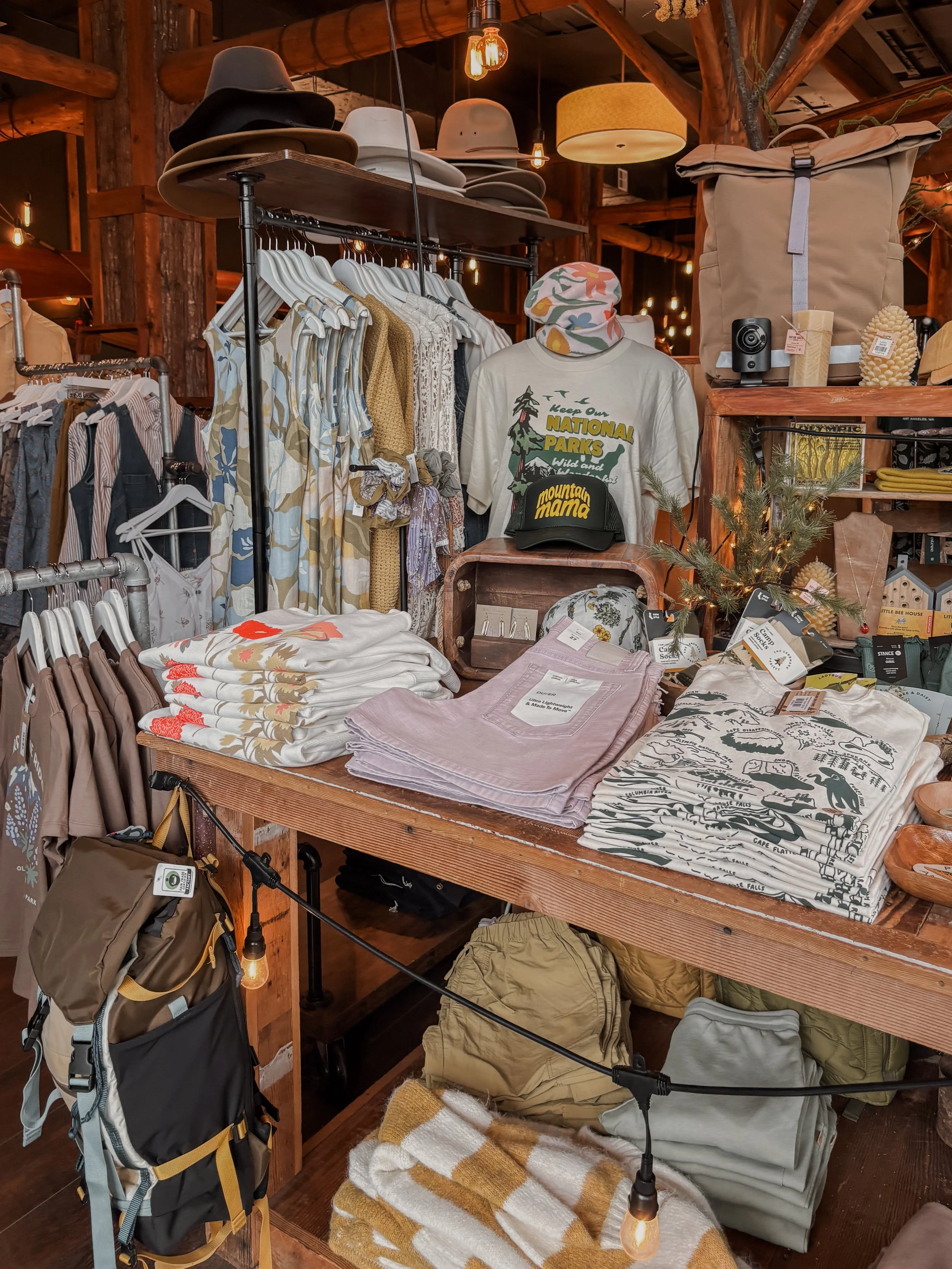 Clothing and accessories display inside MOSS, a store in downtown Port Angeles, with a table with folded shirts, jackets, hats, books, and camping gear.