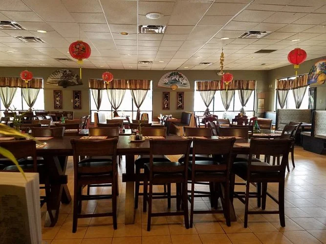 Empty restaurant dining area decorated with red Asian lanterns and framed artwork, with large windows covered by curtains.