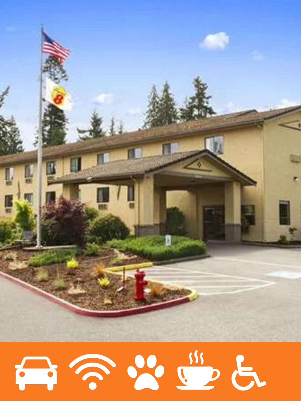 Exterior of a yellow motel or hotel building with a parking lot, American flags, and surrounding greenery, under a partly cloudy sky.